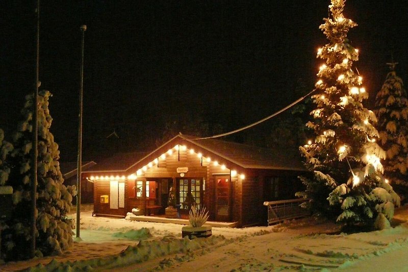Winterliches Holzhaus mit verschneitem Dach und festlicher Beleuchtung.