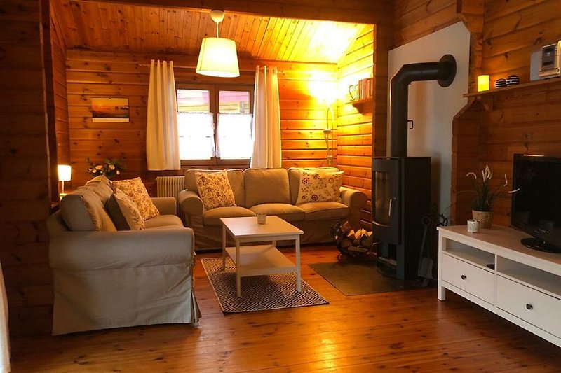 Bsp. Ferienhaus LTD 43 - Gemütliches Wohnzimmer mit Holzmöbeln, bequemer Couch und stilvoller Beleuchtung.