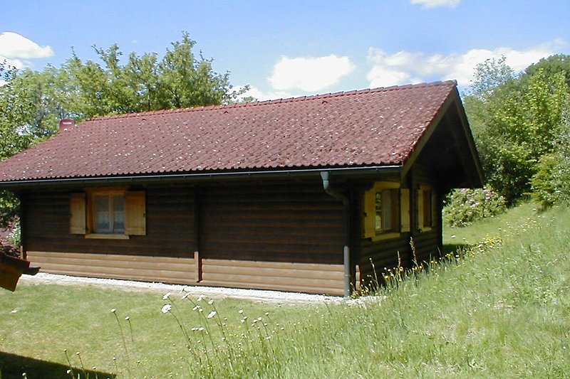 Rustikales Holzhaus mit grünem Garten und blauem Himmel.
