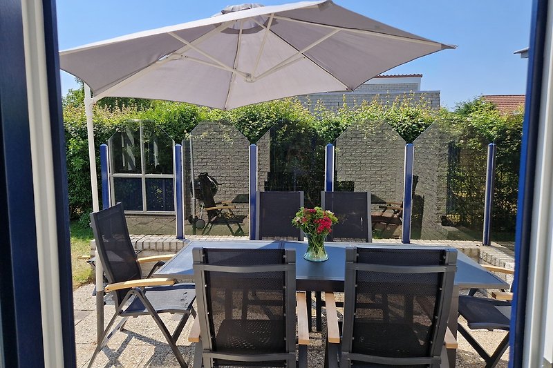 Sonnige Terrasse mit Pflanzen, Möbeln und Sonnenschirm.