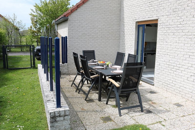 Ferienhaus mit Tisch, Stühlen, Pflanzen und Zaun.