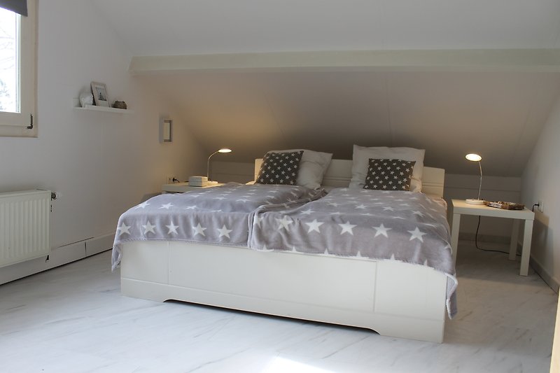 Gemütliches Schlafzimmer mit Holzbett, grauem Bettzeug und Fenster mit Jalousien.
