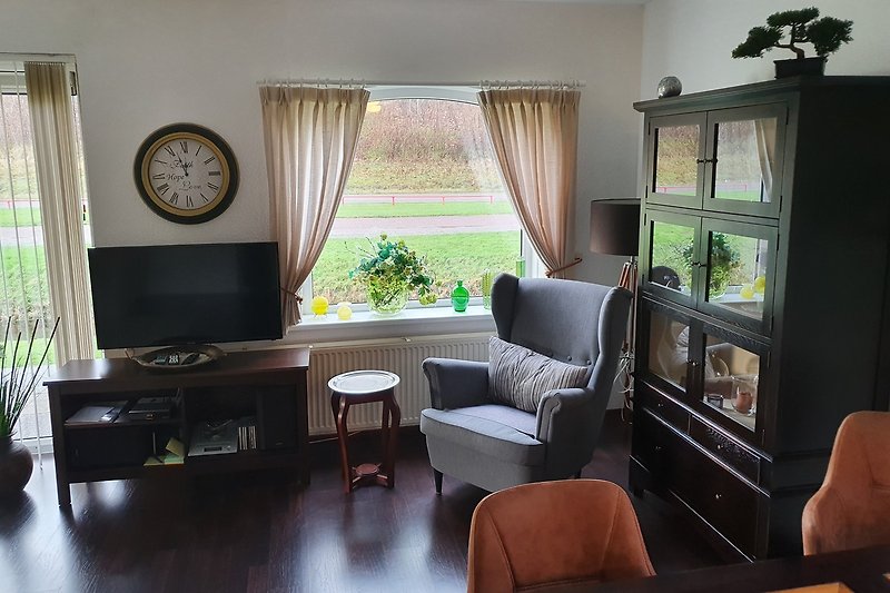 Modernes Wohnzimmer mit eleganten Möbeln, Pflanzen, Uhr und Fernseher.