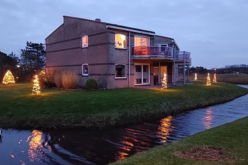 Haus am See mit Garten, Bäumen und Abendhimmel.