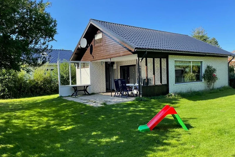 Gemütliches Haus mit Garten und Veranda, umgeben von grüner Landschaft.