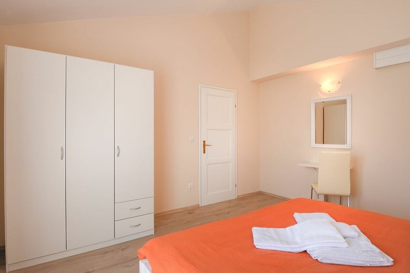 Gemütliches Schlafzimmer mit Holzmöbeln und orangefarbenen Textilien.