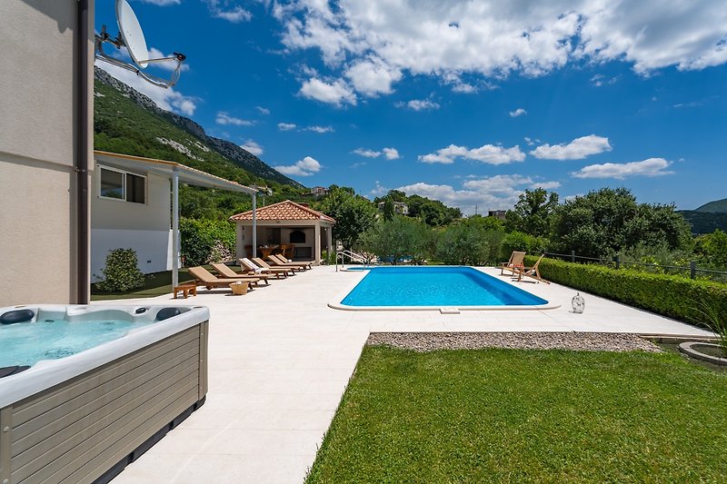 A beautiful house with a swimming pool, surrounded by lush greenery and outdoor furniture.