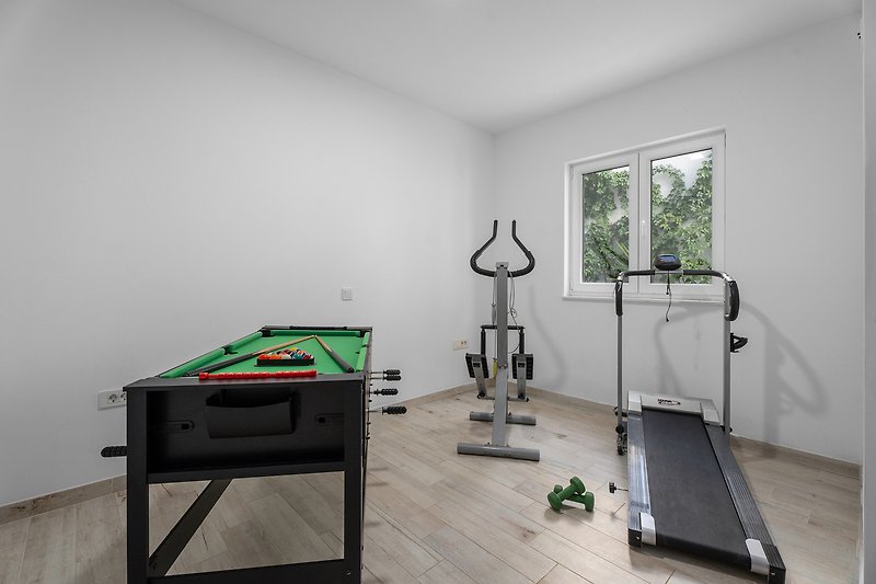 Fitnessraum mit Laufband, Orbitrek, einigen Gewichten und Multi-Combo-Spieltisch