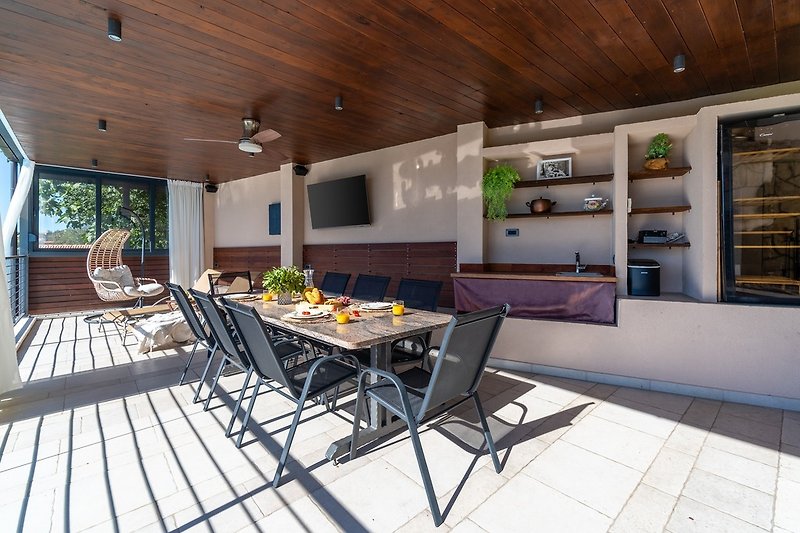 Der Außenbereich bietet einen überdachten Essbereich und eine Sommerküche mit TV, Kühlschrank und Eismaschine