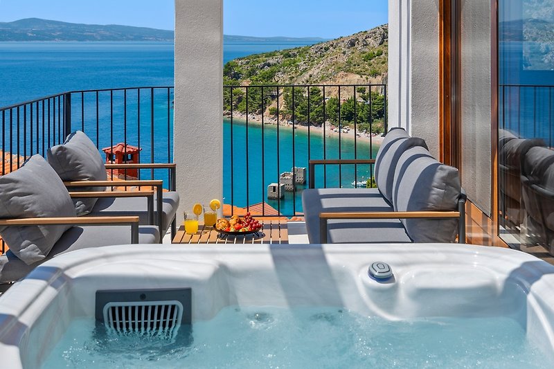A Terrace wit a Hot-tub, 2 sun deck chairs, and a lounge corner and panoramic sea and island views.
