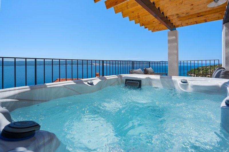 A Terrace wit a Hot-tub, 2 sun deck chairs, and a lounge corner and panoramic sea and island views.