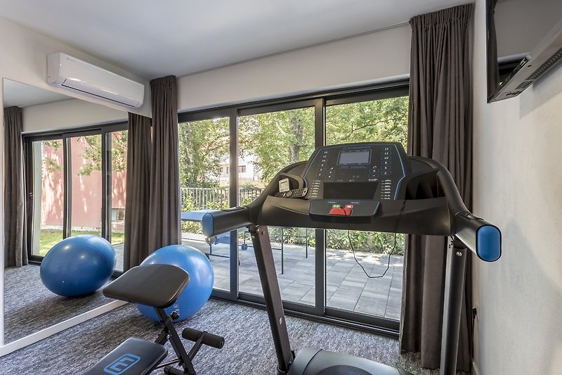 Fitnessraum mit einem Indoor-Laufband, Gewichten, einer Bank, einem Fernseher und einer Klimaanlage