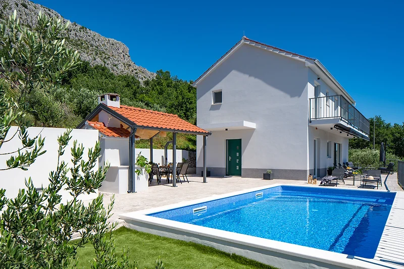 Villa mit Pool, Palmen, Bergen und stilvollen Gartenmöbeln.