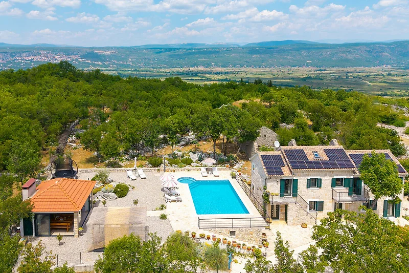 Villa mit Pool, Sonnenliegen und Sonnenschirm im grünen Umfeld.