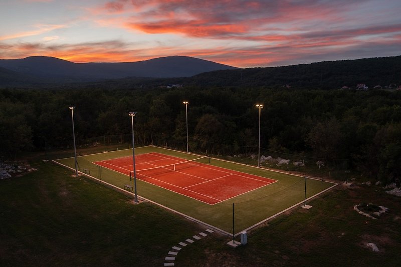 Ein Tennisplatz im Freien mit Kunstrasen und Tennisausrüstung sowie Beleuchtung für abendliches Spielen