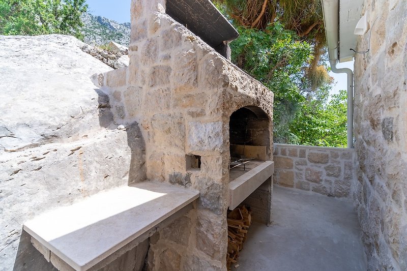 A traditional barbecue is located next to the main entrance to the house, next to the outdoor dining area.