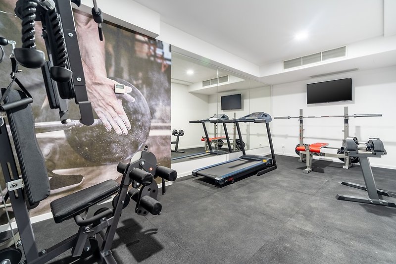 well-equipped gym with Treadmill, a Multifunction device, Bench with some weights, a TV