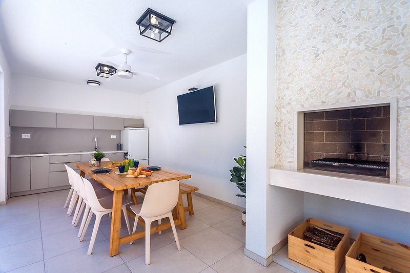 Eine voll ausgestattete Sommerküche mit TV, Kühlschrank, Grill und Essbereich für 10 Personen
