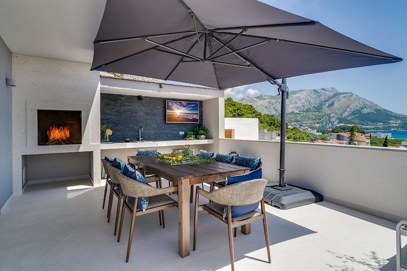  An outdoor dining area with a dining table for 8 people with a barbecue, a TV and a fridge 