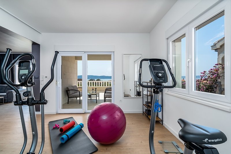 Next to it is a small gym area with Orbitrak, Exercise bike, yoga mats and weights