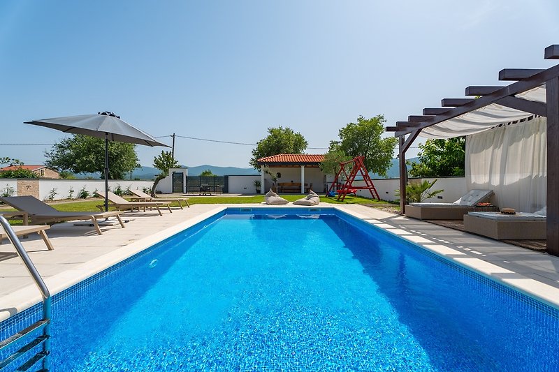 A stunning property with a swimming pool, azure sky, and lush green landscape.