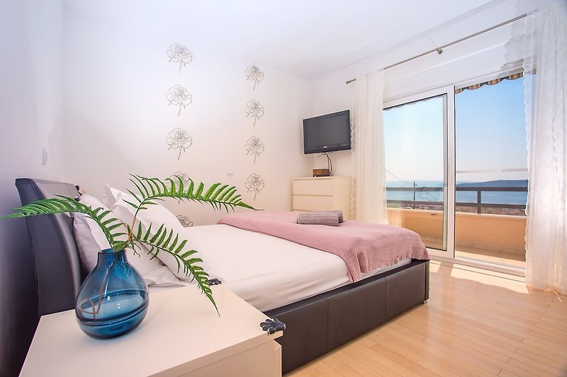  Schlafzimmer Nr. 1 mit einem 180 x 200 cm großen Kingsize-Bett, einem TV und einem Balkon mit Meerblick.