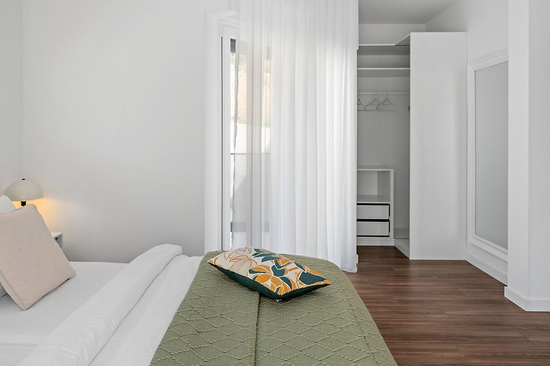 Modernes Schlafzimmer mit Holzbett, Lampen und grauen Textilien.