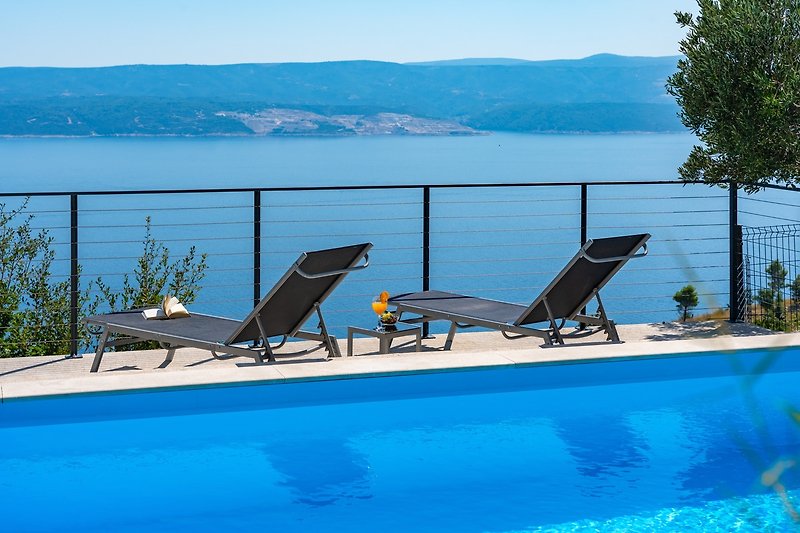 Relax by the pool in this stunning seaside resort with beautiful landscape and outdoor furniture.