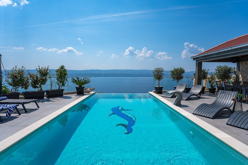 Luxuriöser Poolbereich mit Palmen, Sonnenliegen und Meerblick.