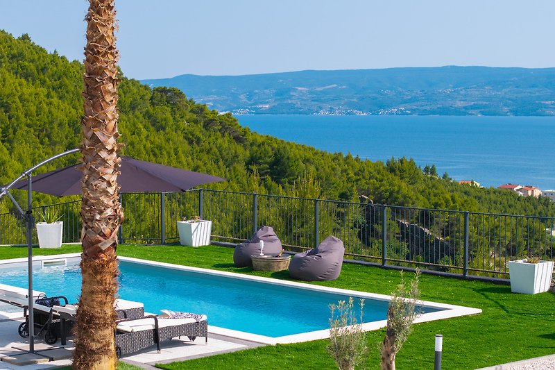 Villa mit Pool, Palmen, Sonnenliegen und schattiger Terrasse.