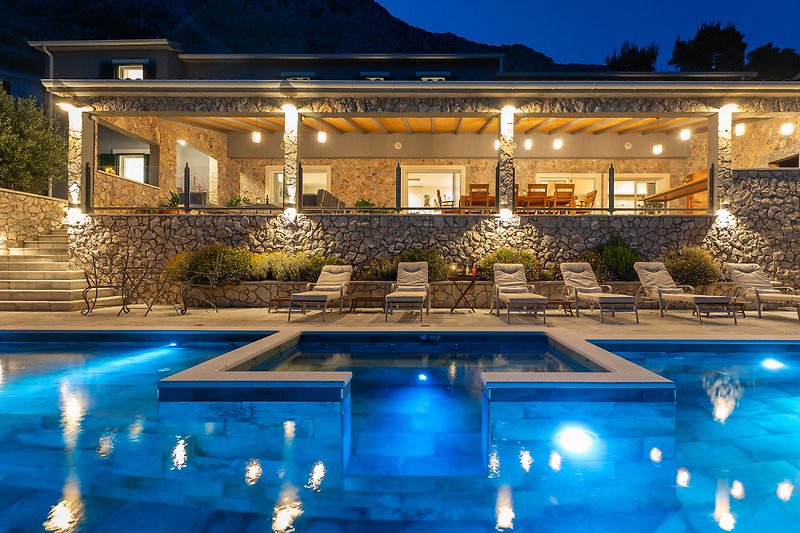 Luxuriöse Villa mit Pool, Palmen und stilvoller Beleuchtung bei Nacht.