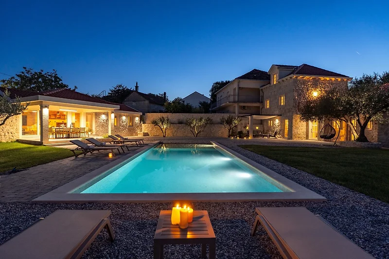 Beleuchteter Pool mit Wasserbecken, Liegen und Blick auf die Villa.