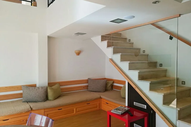 Woonkamer met een moderne inrichting, inclusief een comfortabele grijze bank, een houten koffietafel en een groot raam dat veel natuurlijk licht binnenlaat. De muren zijn neutraal van kleur, wat een rustgevende sfeer geeft.