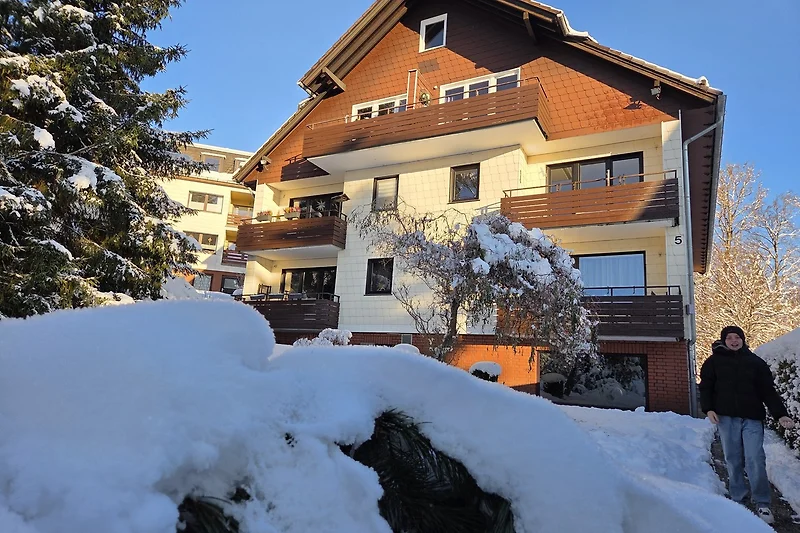 Verschneite Tannen und ein Haus im winterlichen Bergdorf am Skigebiet.