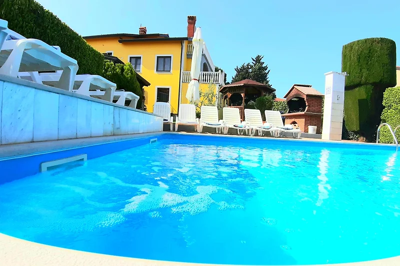 Feriemhaus mit Pool, Sonnenliegen, Sonnenschirmen und Palmen.