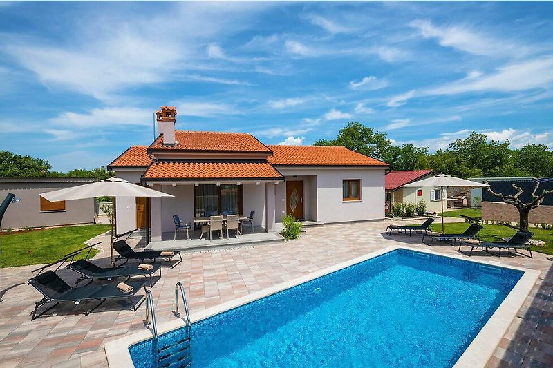 Schönes Haus mit Pool, blauem Himmel und grüner Landschaft.