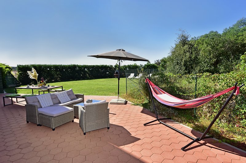 Sonnige Terrasse mit Liegestuhl, Hängematte und Garten.