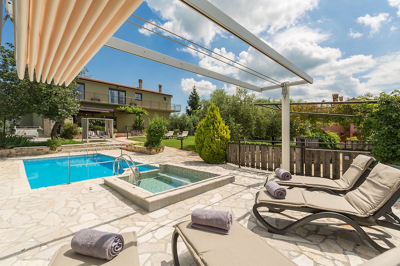 Villa mit Pool, Sonnenliegen und üppiger Landschaft.