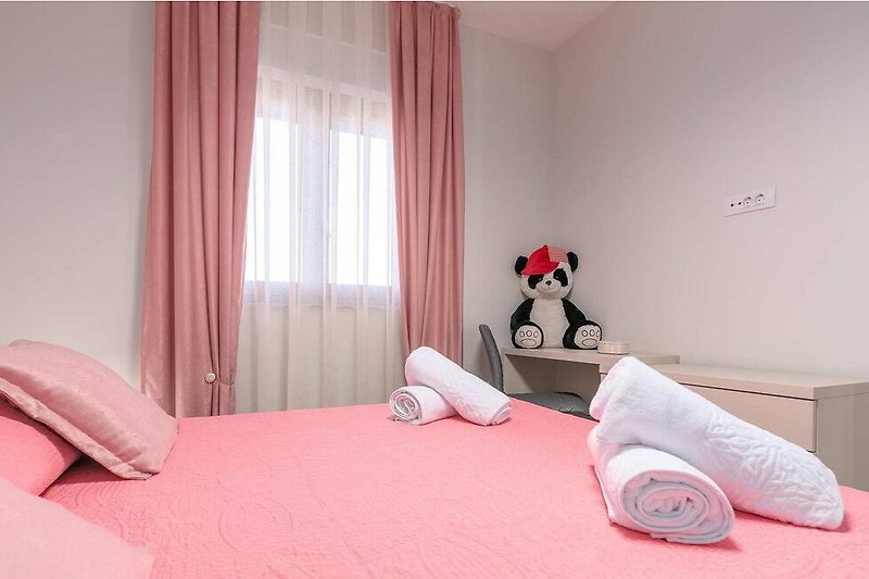 Gemütliches Schlafzimmer mit rosa Vorhängen, Bettwäsche und Holzmöbeln.