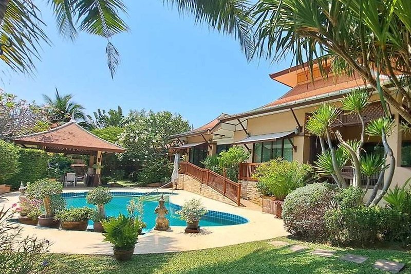 Schwimmbad umgeben von Palmen, Grünflächen und blauem Himmel.