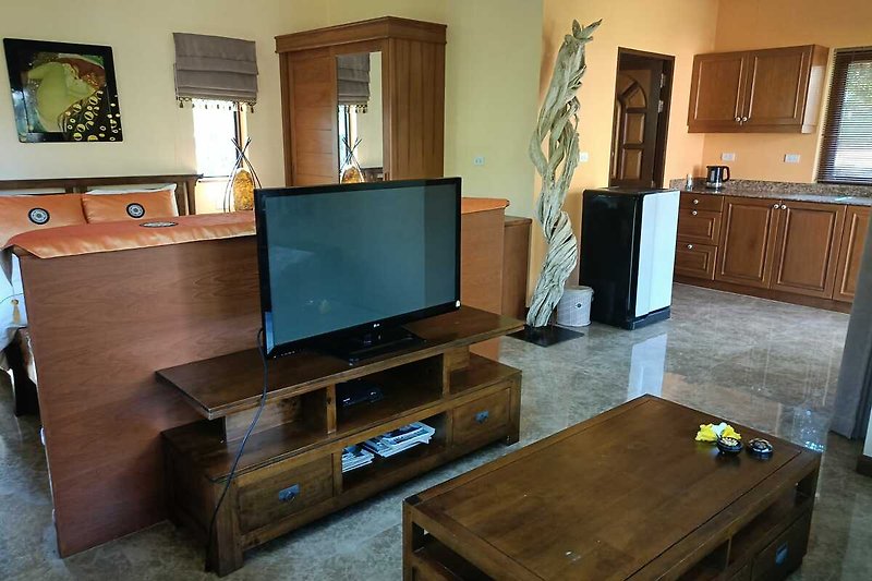 Wohnzimmer mit Fernseher, Holzmöbeln und gemütlicher Einrichtung.