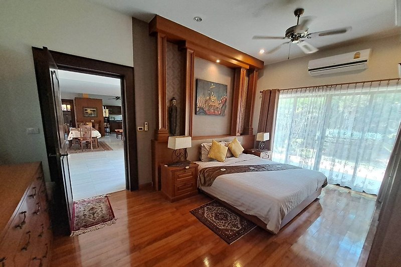 Schlafzimmer mit Holzmöbeln, Deckenventilator und gemütlicher Beleuchtung.