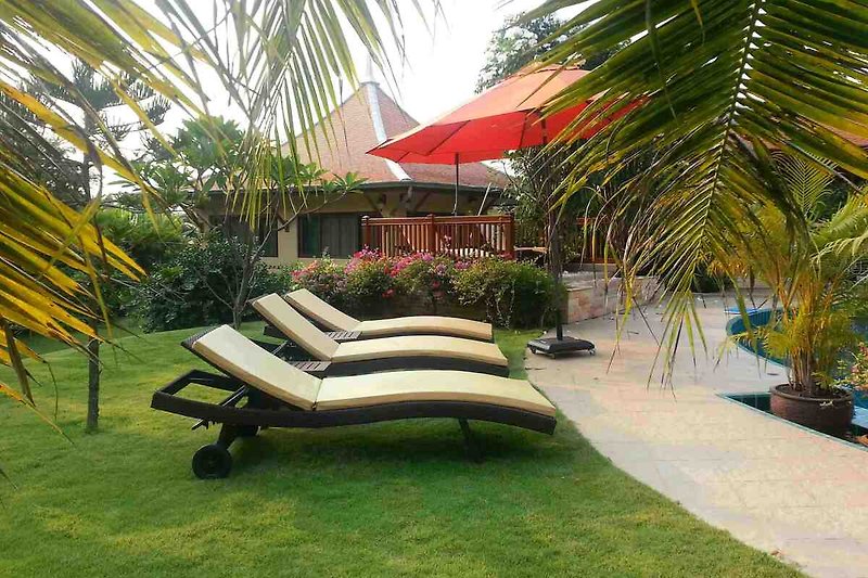 Schwimmbad mit Sonnenschirm und Liegestuhl unter Palmen.