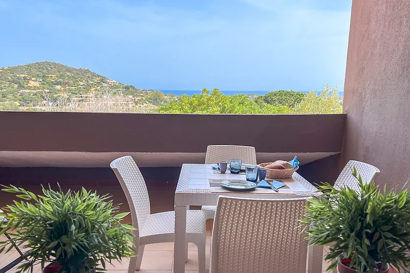 Balkon mit Outdoor-Möbeln, schattigem Tisch und grünen Pflanzen.