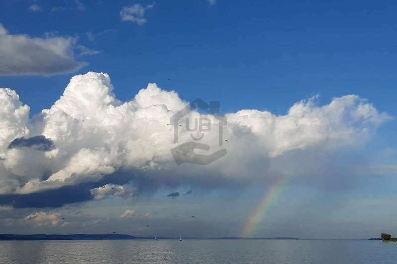 Malerischer See mit Regenbogen, ruhigem Wasser und blauem Himmel.