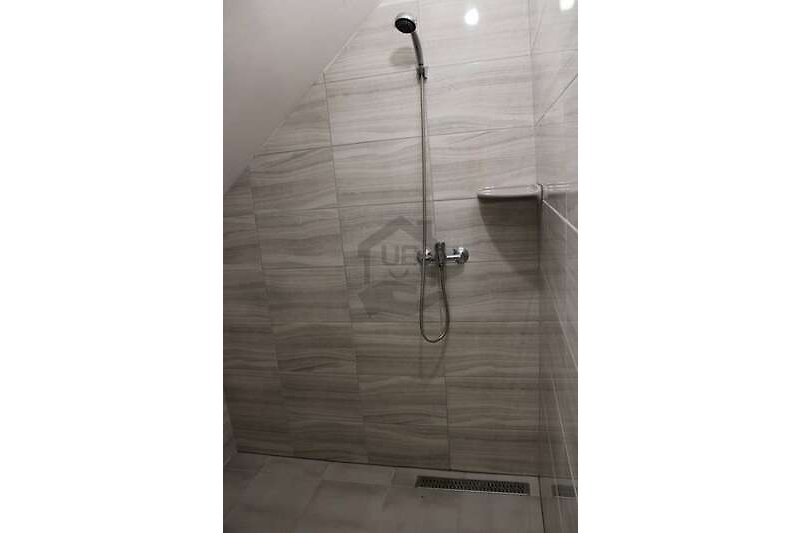 Badezimmer mit Dusche, Holzboden und moderner Armatur.