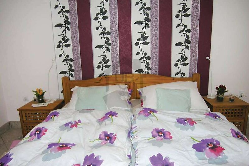 Gemütliches Schlafzimmer mit lila Bettwäsche und Holzmöbeln.