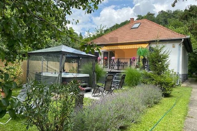 Gemütlicher Garten mit Bäumen, Sträuchern und Gartenmöbeln.