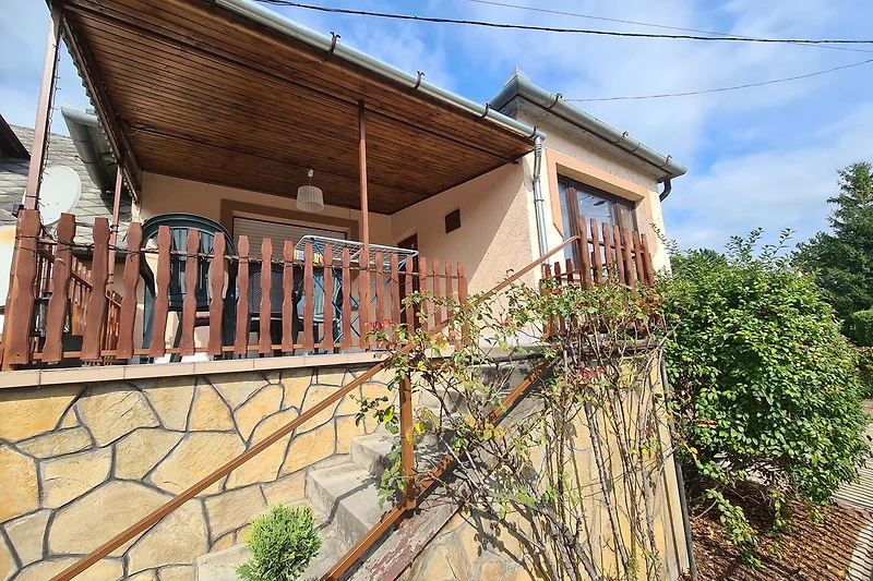 Haus mit Balkon, Garten, Einfahrt, Zaun und schöner Veranda.