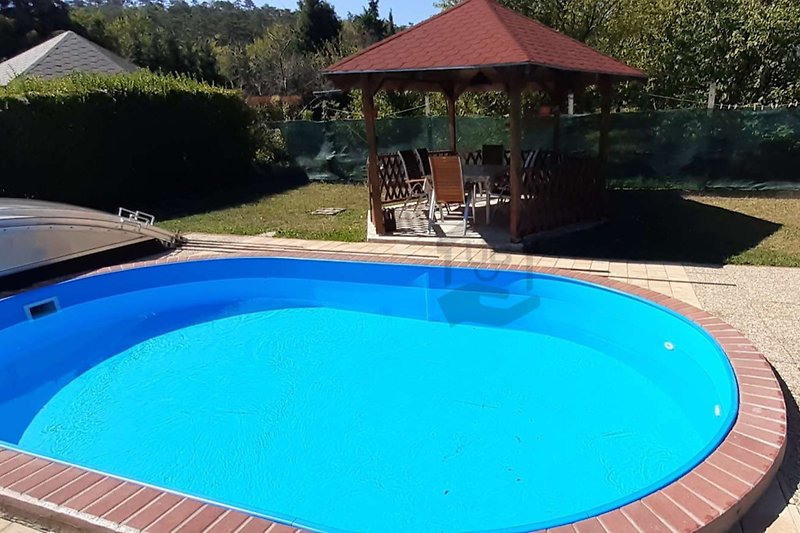 Schwimmbad mit blauem Wasser, grüner Landschaft und bequemen Außenmöbeln.
